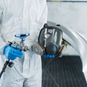 Сlose-up view of car painter with paint gun and protective respirator in hands.
